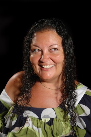 Image of Patty Berne, a Japanese-Haitian queer disabled woman. She has long curly dark hair and is smiling widely and looking to the right of the camera. She is wearing an off-the shoulder shirt in a white, navy, and green pattern. Image credit Richard Downing courtesy of Sins Invalid.