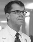 Profile of a middle aged white man wearing a white shirt and dark tie. The photo is in black and white. He is wearing glasses and has short hair.